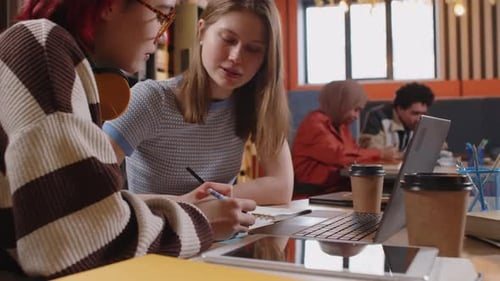 Gen Z Female Students Taking Notes in Workbook and Talking in College Library