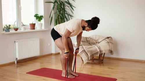 Mixed Race Sportsman is Training with Rubber Bands Tensing Muscles of Arms Using Legs