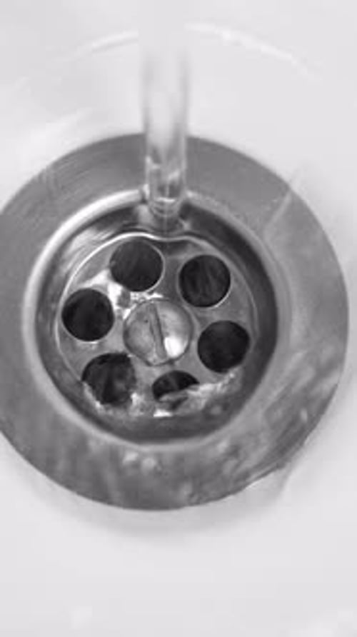 Water flows into a metal drain, close up