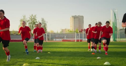 Youth Soccer Players in Red Uniforms Sprint Through Cone Drills on a Sunny Grass Field During Team