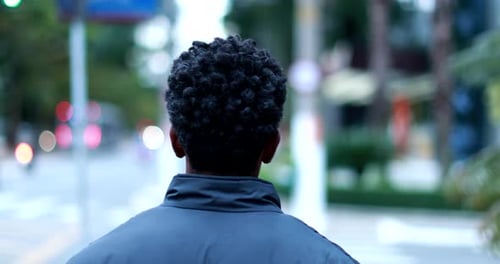 Back of man walking in city street, african american person walks in urban sidewalk commuting
