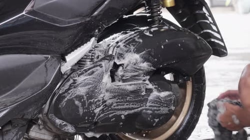 Person Washing a Shiny Black Motor Scooter