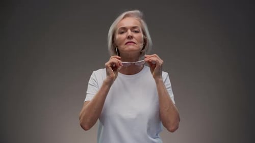 Senior Woman Puts on Glasses in Studio
