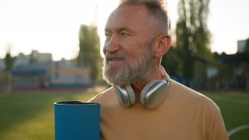 Adult Smiling with Yoga Mat on Sports Field