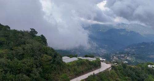 A stunning aerial shot captured by a drone showcasing mist-covered mountains, a winding road, and a