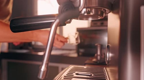 Barista placing glass measuring cup on espresso machine grate under group head, close up view with