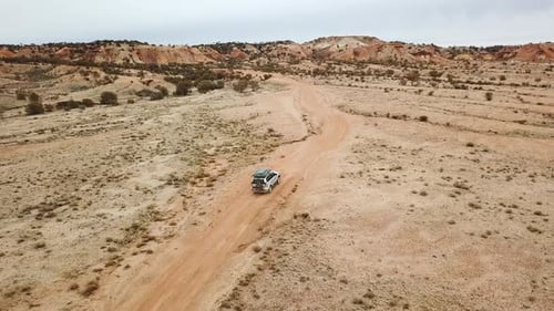 Aerial tracking offroad vehicle on remote dirt road leading into colorful desert hills