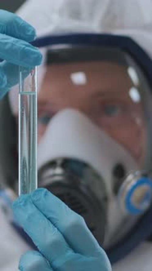 Un científico que lleva guantes protectores y una máscara respiratoria examina cuidadosamente los tubos de ensayo en un