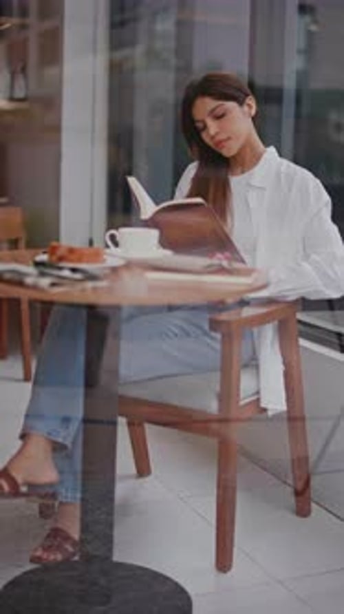 Young Woman Turning Pages of a Book at an Outdoor Bistro Table