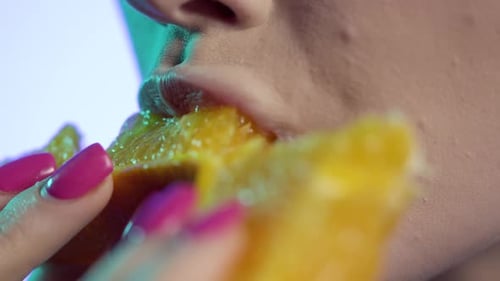 Mulher mordendo uma fatia de laranja com luz verde em um fundo roxo
