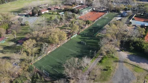 Aerial view of several soccer fields with some people playing inside them, located between trees in