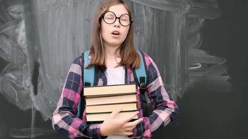 Student Holding Textbooks in Front of Chalkboard