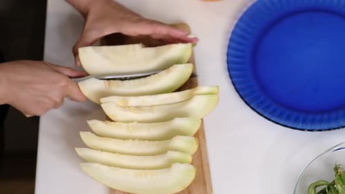 Eine Person schneidet eine Melone in gleichmäßige Stücke mit einem blauen Teller an der Seite. Das Foto hebt die hervor