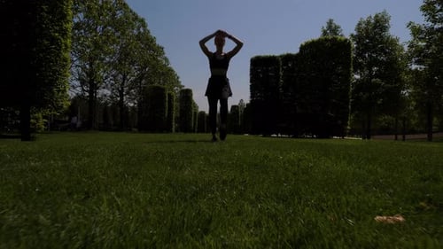 Silhouette of a Young Woman in a City Park She Jumps and Raises Her Hands Up