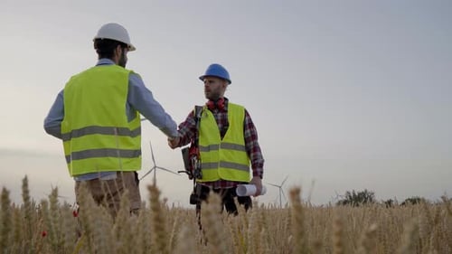 Engineer and Technician Shake Hands to Work on New Sustainable Wind Turbine Project in Field