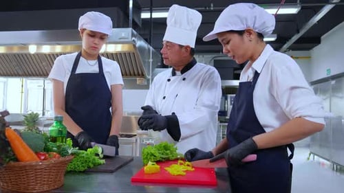 Instrucción y explicación del chef del equipo al aprendiz sobre cómo cocinar y preparar verduras frescas.