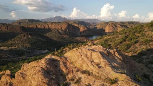 Drone voando em direção a uma pessoa parada na beira de uma montanha na hora dourada olhando para baixo, montanha
