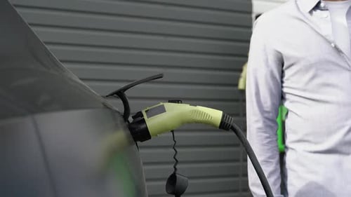 A Man Disconnects a Charging Cable to an Electric Car Close Up