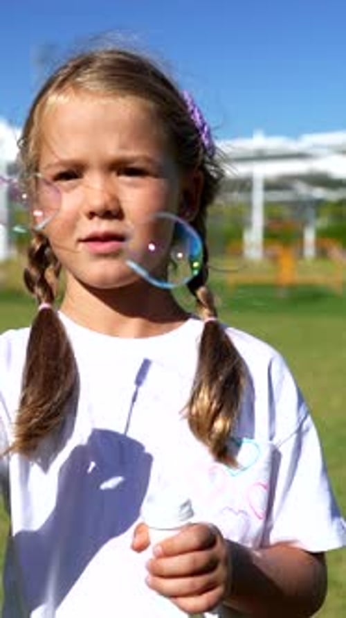 Blonde girl blows soap bubbles in summer sunshine