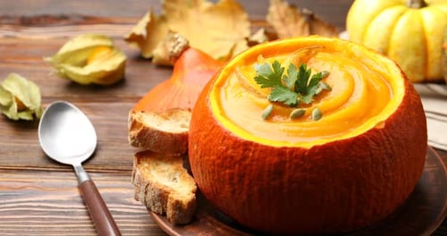 Tasty pumpkin cream soup with seeds and parsley served in pumpkin on wooden table, closeup