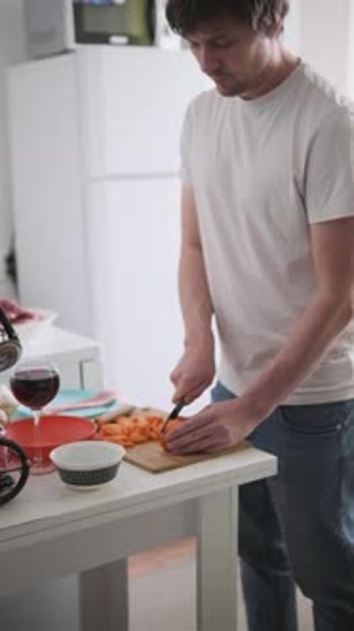 Man Slicing Carrot on Wooden Cutting Board Preparing Fresh Ingredients at Home Kitchen Table
