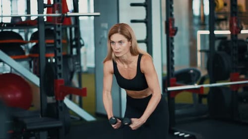 Woman Exercising With Dumbbells in a Gym Setting Focusing on Strength Training