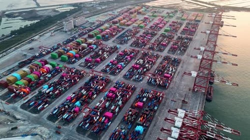 Drohnenansicht des Containerterminals bei Sonnenuntergang mit Kränen und gestapelter Ladung