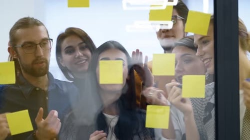 Business Team Brainstorm Writing Ideas on Paper Sticker Notes and Post It on Glass Wall Startup