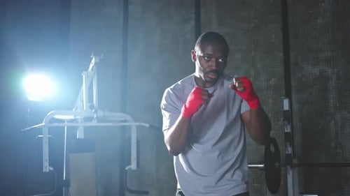 Fitness Workout in Gym African Man Fighter Preparing for Fight Punching with Red Boxing Wraps Sports