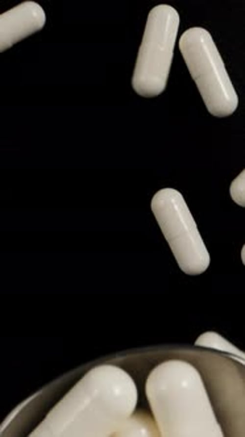 White capsule pills fall on a spoon, black background, top view. Dolly slider extreme close-up. Laow