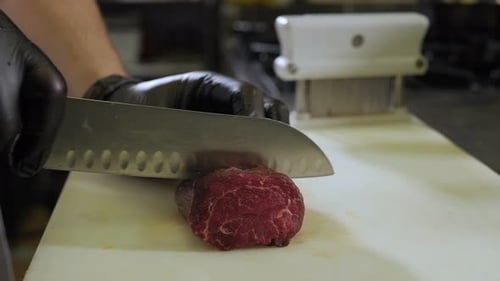 Chef Cutting Beef with a Knife on a Cutting Board in the Kitchen of a Restaurant