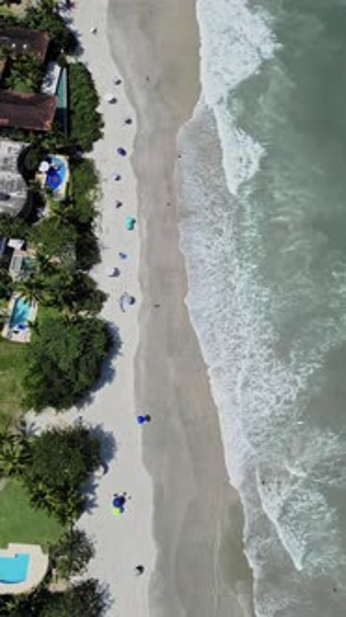 Aerial zoom out drone view of sea water coast with white foaming waves, beach and some vegetation tr
