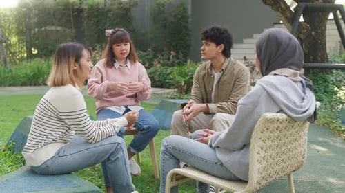 Small Asian group of people sit in a close circle and talk to a therapist in park.