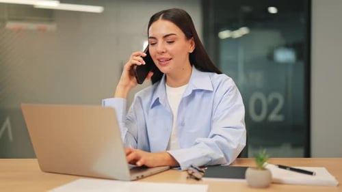 Smiling Woman Working on Laptop and Talking on Phone