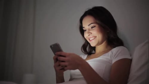 Smiling Woman using Phone in Bed at Night