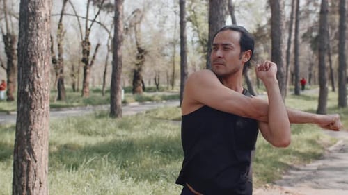 Sportsman Engaging in Arm Stretches While Warming Up in a Lush Green Park
