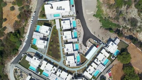 Birds eye aerial view over holiday homes with pools on top of a hill in Greece