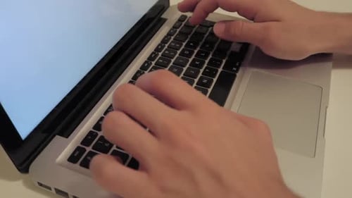 male hands typing on laptop computer keyboard with blank white screen, medium close-up