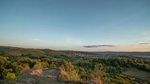 Bewegender Zeitraffer eines Sonnenuntergangs über bewaldeten Hügeln und Dörfern.