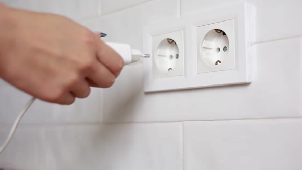 close up of woman's hand plugging white power plug into white multiple ...