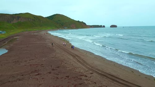 Top view of people walking on north coast with mountains. Clip. Beautiful walk on ocean coast