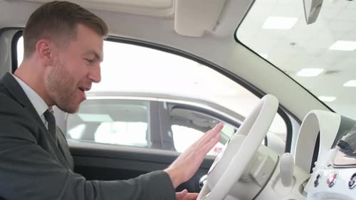 A Happy and Smiling Man is Sitting in the Interior of a New Car at a Car Dealership