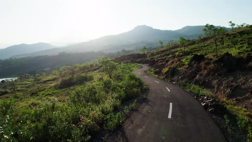Aerial Drone Flying Over Winding Hillside Road at Hazy Sunrise
