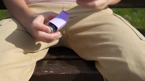 Girl Uses Asthma Inhaler Outdoors on Bench