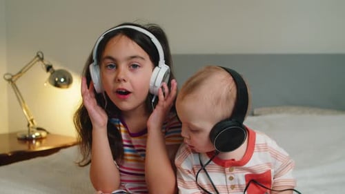 Child and Infant Listening With Headphones on Bed