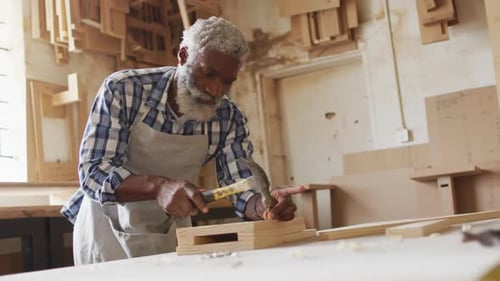 African american male carpenter hammering nails into the wood at a carpentry shop