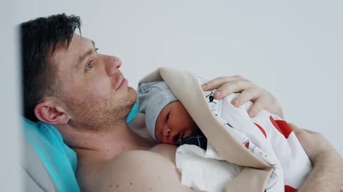 Proud Father Cradling Newborn Baby in Hospital
