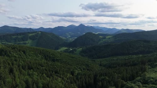 Aerial View of Green Mountain Valley with Forest Hills and Distant Peaks Under Clouds