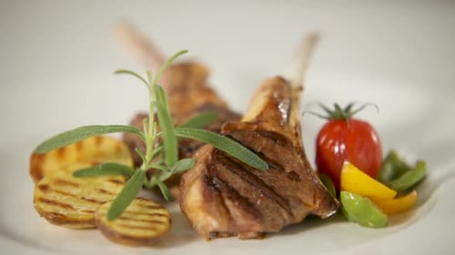 Grilled lamb chops plated elegantly with grilled vegetables and fresh herbs, close-up