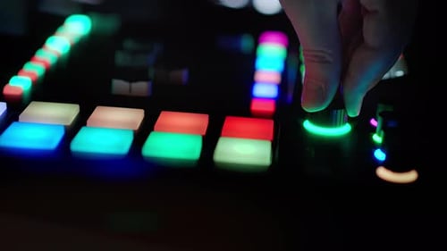 Close-Up of Hands Adjusting Controls on a Glowing DJ Midi Controller